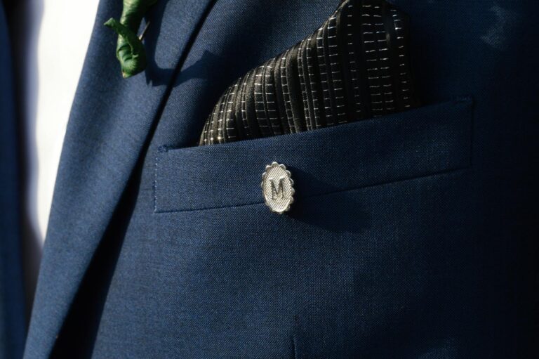 Close-up shot of a navy suit with a monogrammed pin and patterned pocket square.
