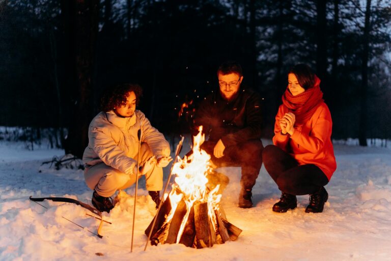 Three friends enjoying a cozy campfire in a snowy forest, surrounded by winter's chill.