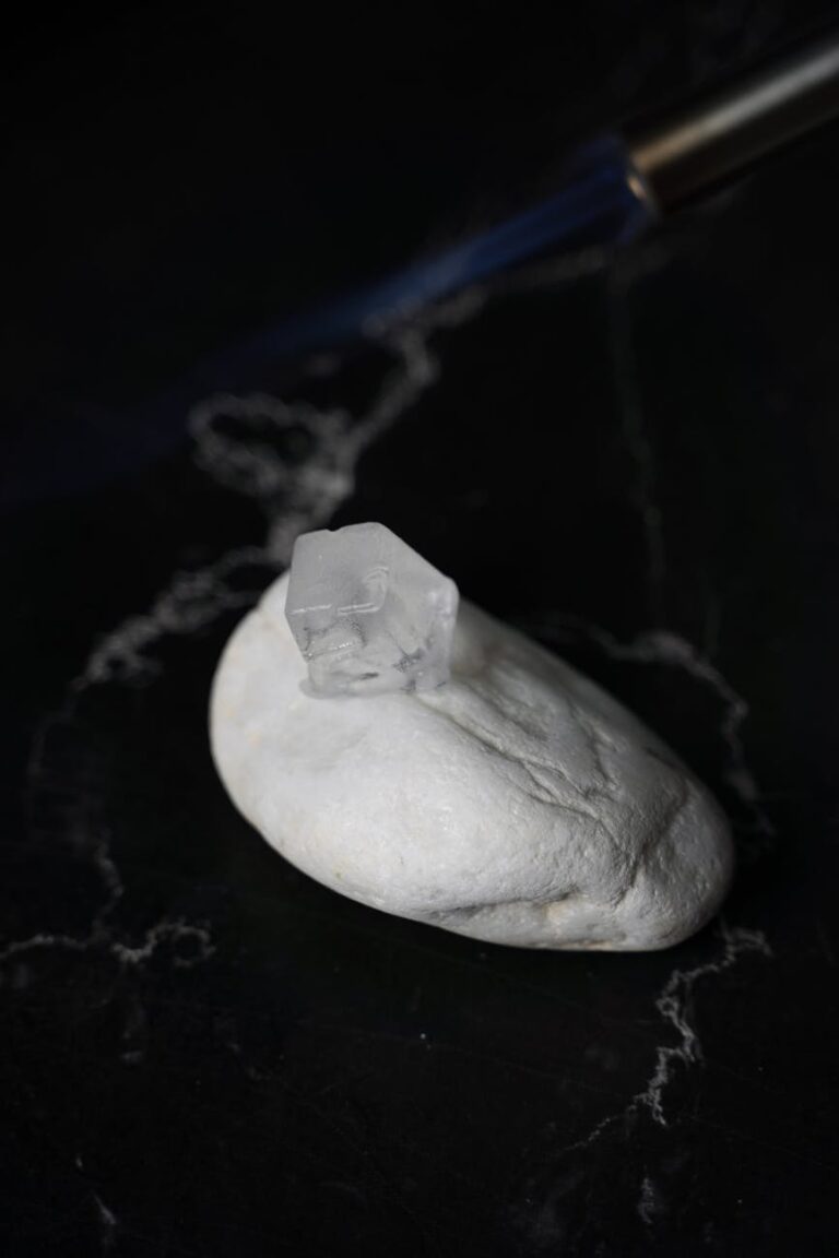 A close-up photo of an ice cube on a white rock with a subtle flame in the background, creating a contrast.