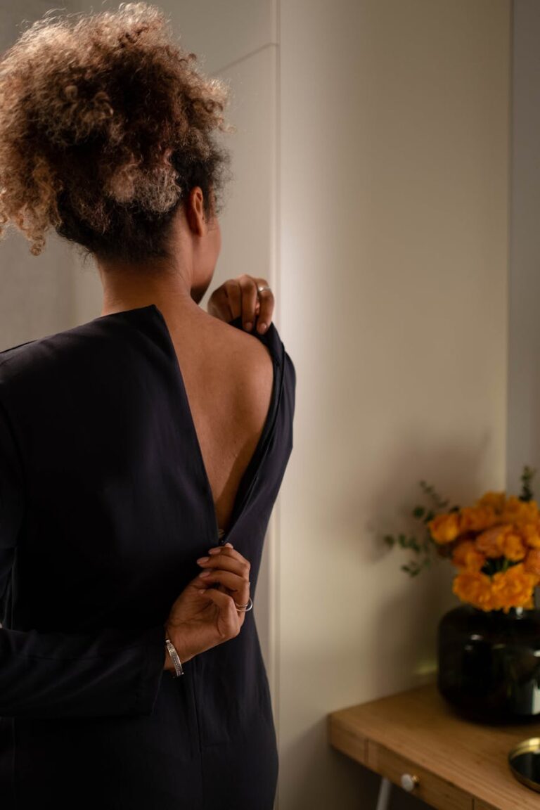 A woman gently unzipping her dress, revealing her back, in a warmly lit room.