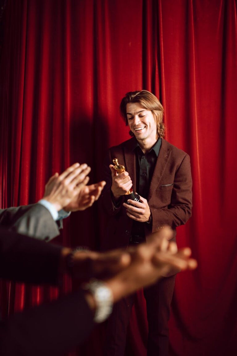 A delighted man in formal wear holding an award, applauded by an audience.