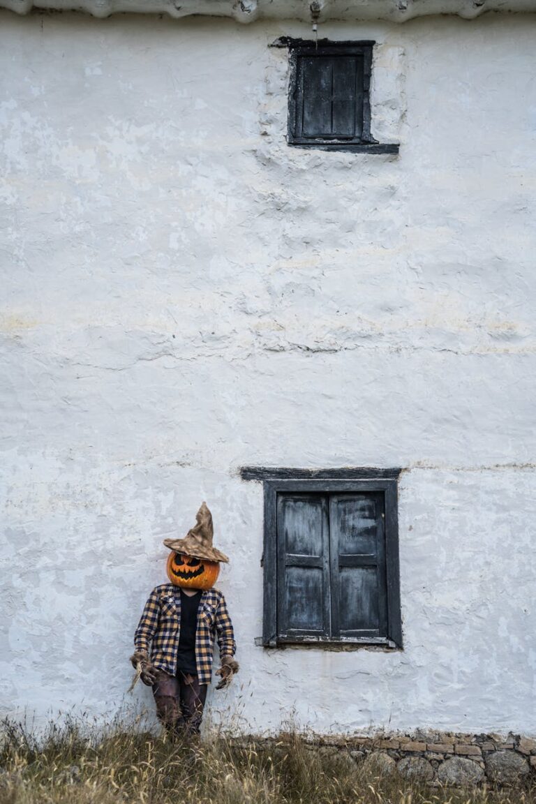 A man with a pumpkin head stands by a rustic wall in Guasca, Colombia, creating a spooky Halloween scene.