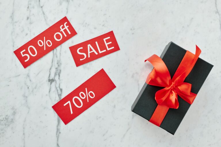 Stylish black gift box with red ribbon and sale tags on marble, perfect for Black Friday promotions.