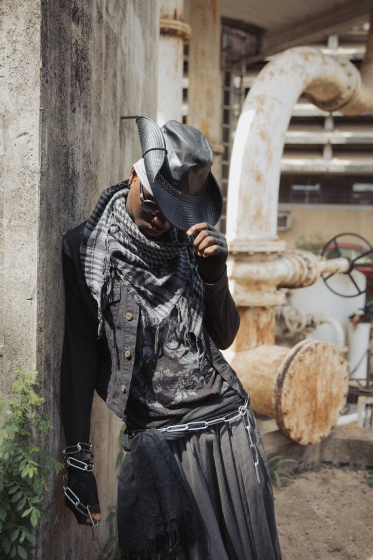 A person in stylish attire posing in an urban industrial setting.
