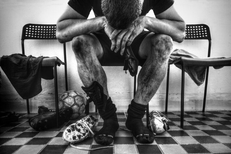 Monochrome image of exhausted soccer player resting in locker room.