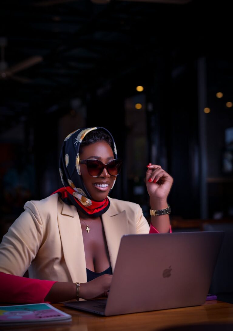 Stylish woman with laptop, wearing sunglasses and scarf, working indoors.