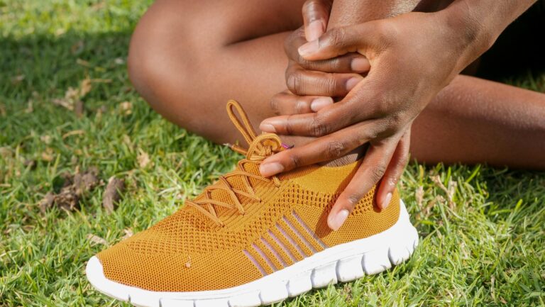 Close-up of athlete holding ankle with running shoe on grass, indicating pain or injury.