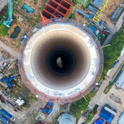 Aerial perspective of a cooling tower in an industrial area, highlighting complex machinery and structures.