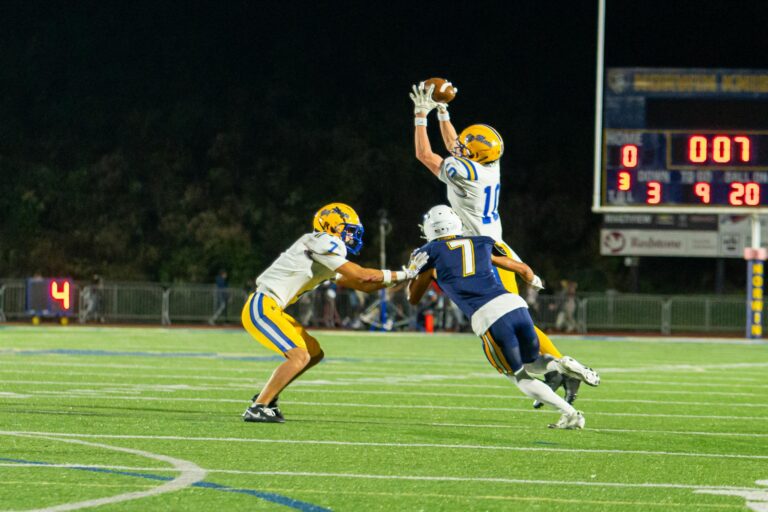 High school football players in a dramatic mid-air catch during a night game.