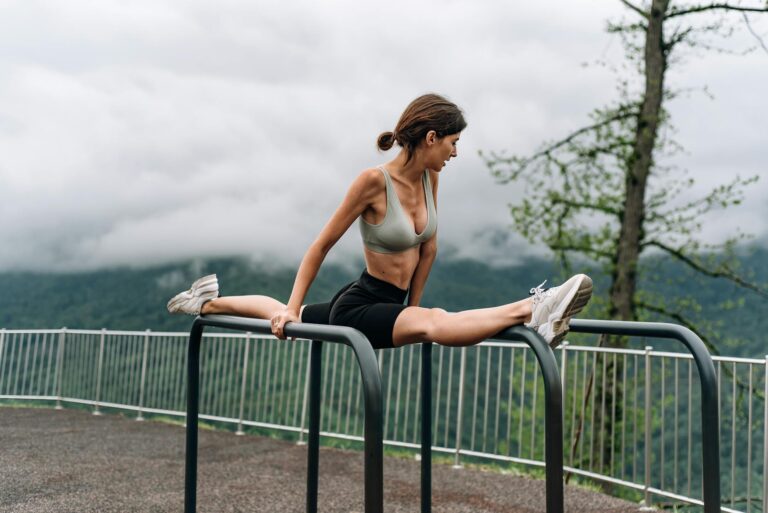 A woman in sportswear performing a split outdoors on metal bars, showcasing flexibility and strength.