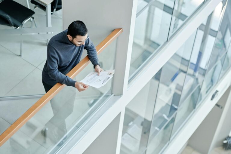 A professional man examines papers in a bright, contemporary office space with glass walls.