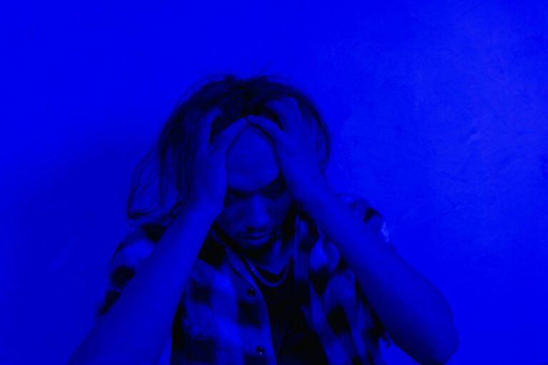 Portrait of a distressed person under dramatic blue lighting, expressing mental anguish.