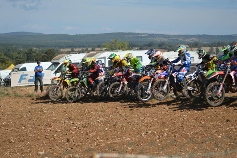 Riders in colorful gear race through a dirt track, showcasing speed and skill in an off-road competition.