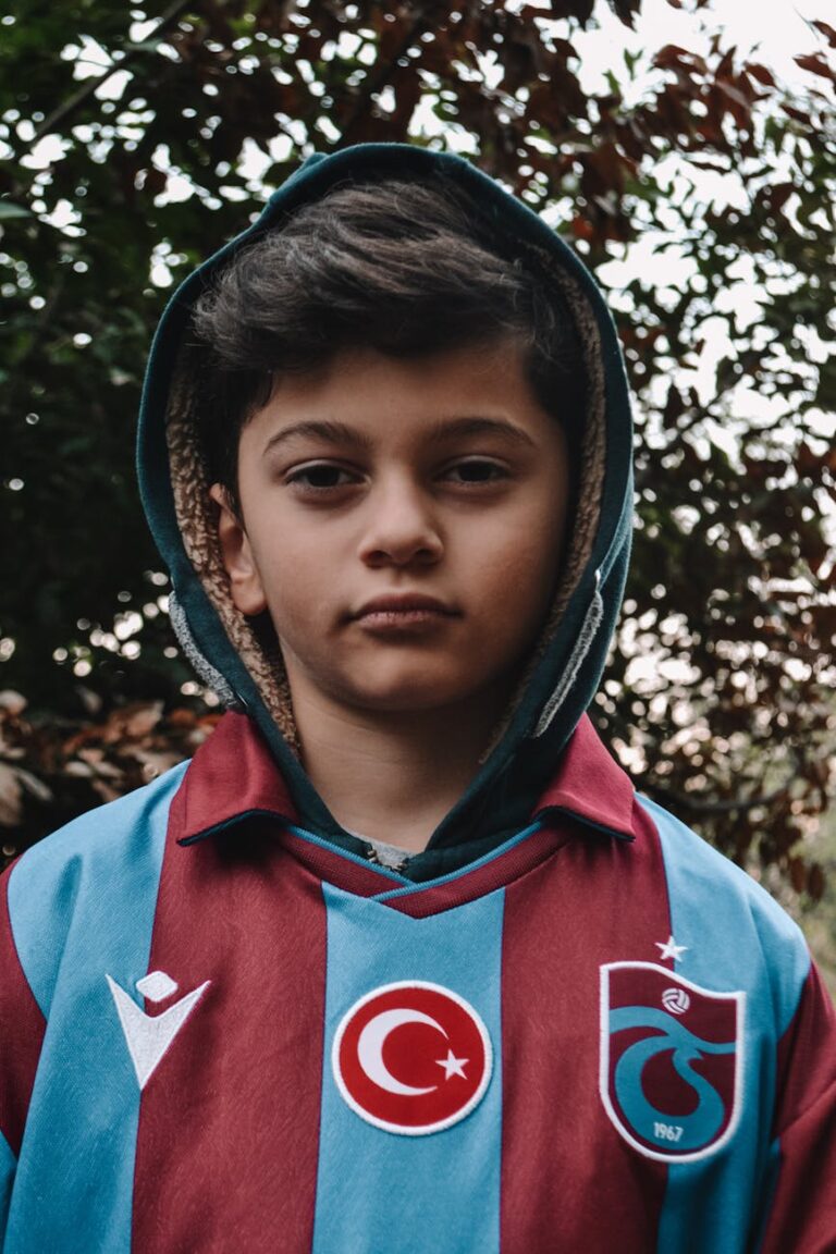 Young boy wearing a sports jersey, standing outdoors with a serious expression.