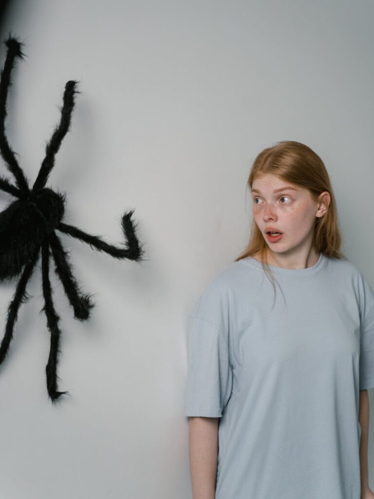 A woman reacts with fear to a large spider on the wall, conveying anxiety and phobia.