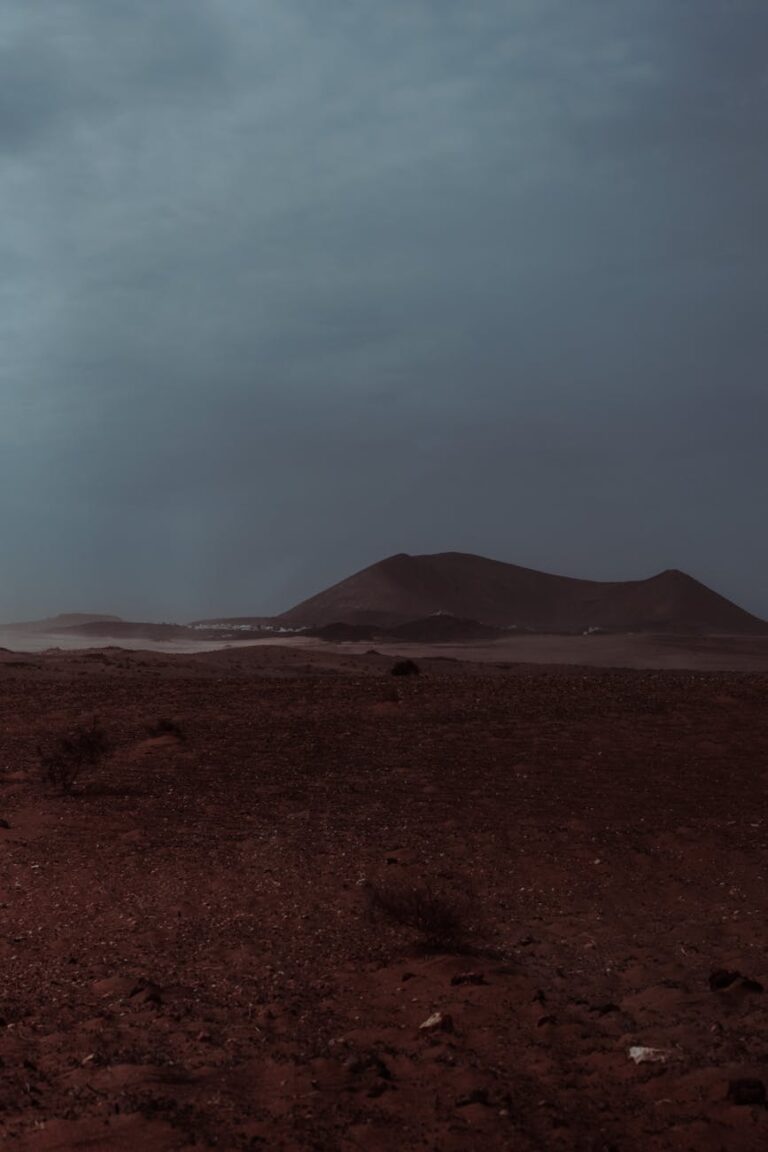 A moody desert landscape with mountains under a dark sky at dusk.