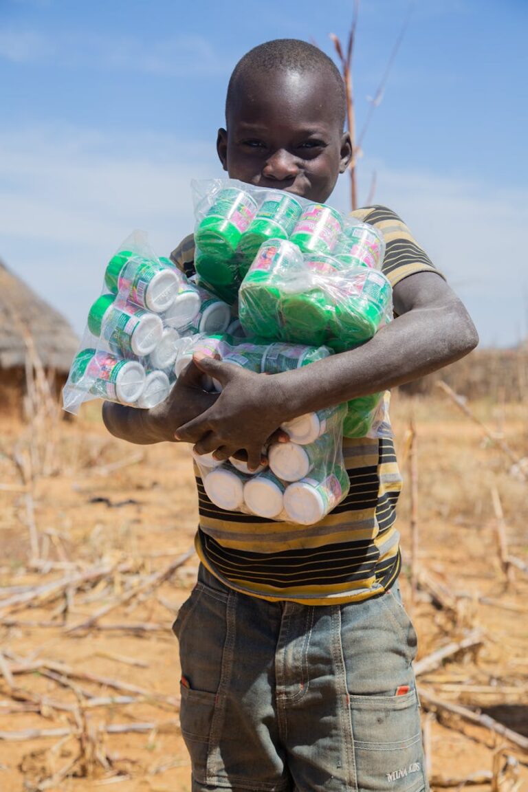 A cheerful boy carries multiple packs of bottled milk outdoors under a clear sky.