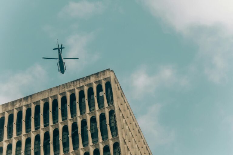 A helicopter soaring above a modern building under a clear blue sky, representing urban exploration.