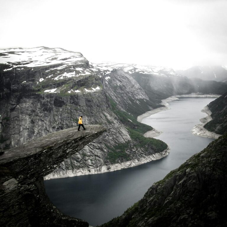 Dramatic view of a hiker on Trolltunga cliff with a breathtaking Norwegian fjord backdrop.