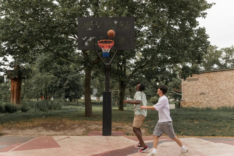 Two young men enjoy a game of basketball on an outdoor court surrounded by greenery.