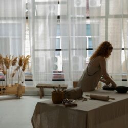 Side view faceless female wearing apron placing clay slab on baking pan while making earthenware in contemporary studio