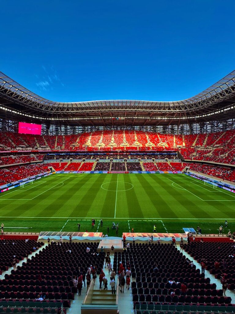 Expansive view of a modern stadium filled with fans under a clear blue sky.