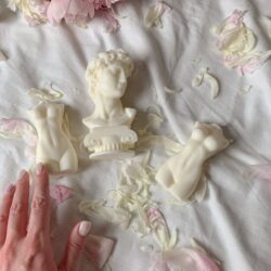 Sculptural soaps arranged on rose petals with a woman's hand touching for decorative effect.