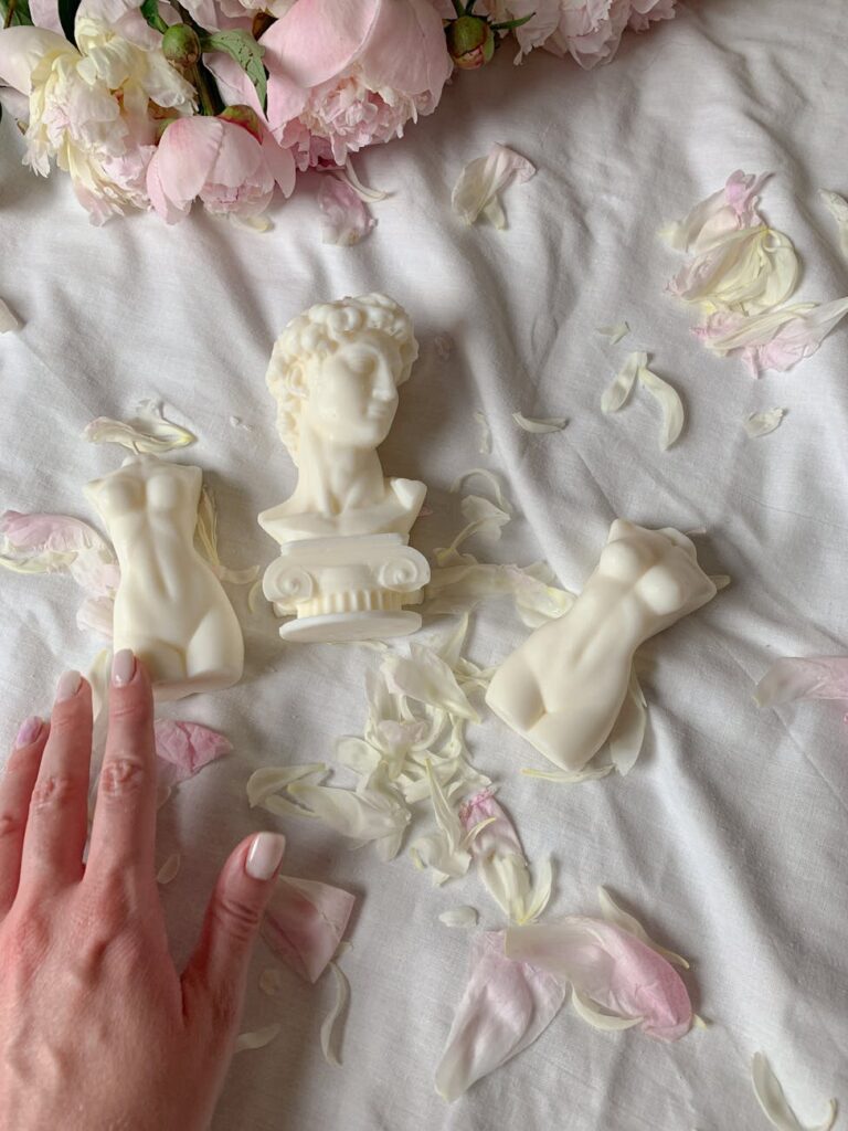 Sculptural soaps arranged on rose petals with a woman's hand touching for decorative effect.