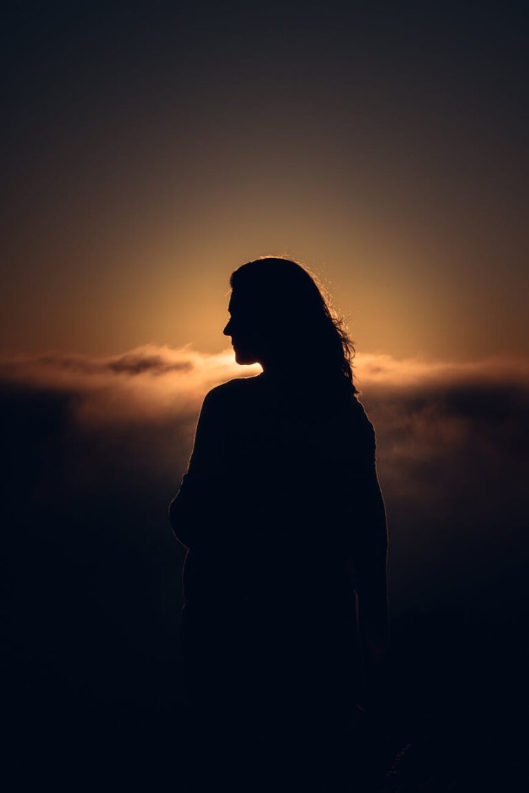 A mysterious silhouette of a woman against a vibrant sunset sky with clouds.