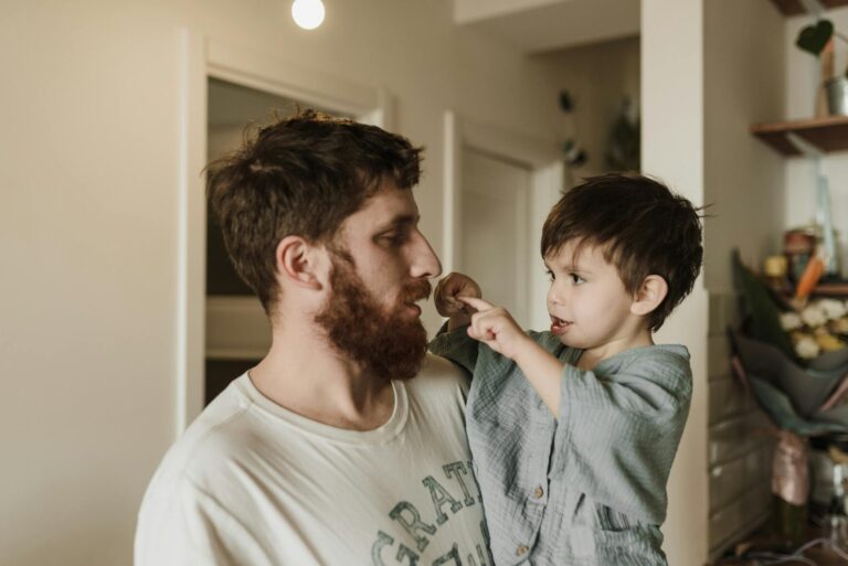 A father with a beard and his young son share a loving and playful moment at home.