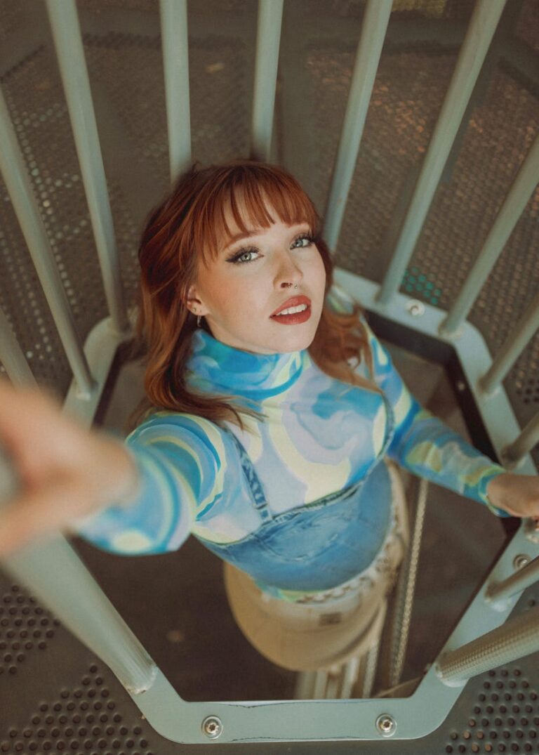 High angle photo of a redheaded woman reaching out from a spiral staircase.