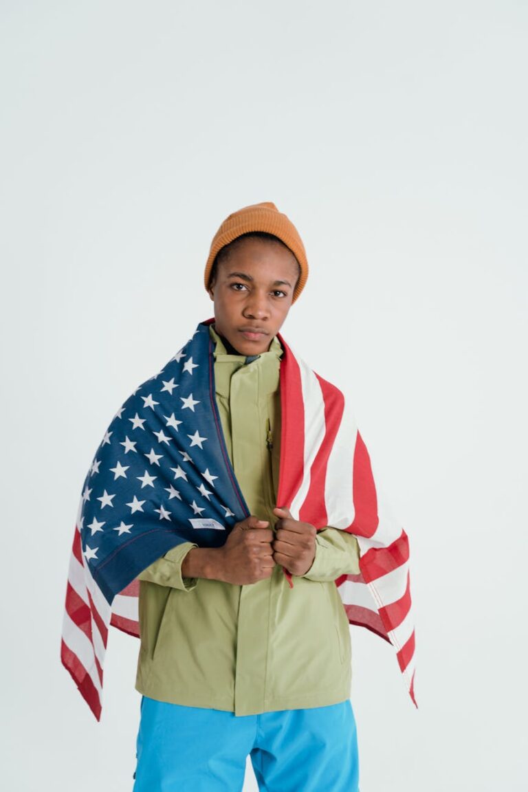 Young individual wearing a winter jacket and beanie wrapped in the USA flag.