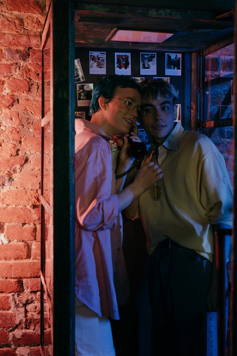 Two teenagers sharing a moment in a vintage telephone booth illuminated by neon lights.