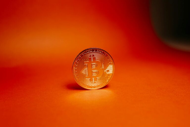 Close-up of a gold Bitcoin coin on a bright orange background, representing cryptocurrency.