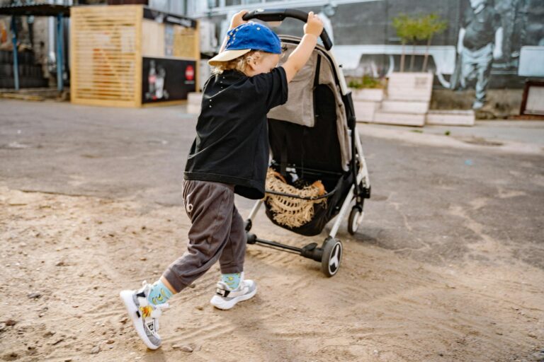 A young boy in a blue cap enthusiastically pushes a stroller on a sunny day.