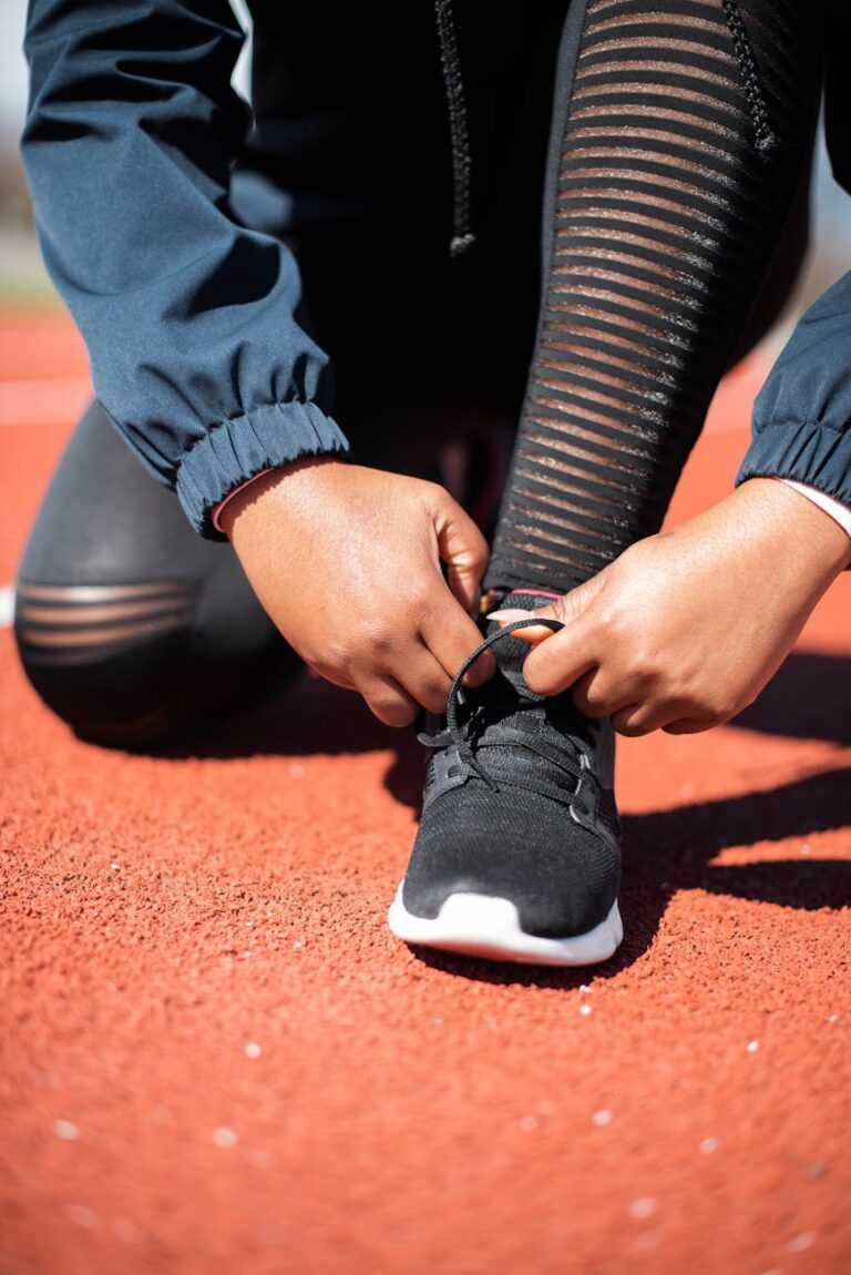 Hands tying shoelaces on running track, preparing for workout.
