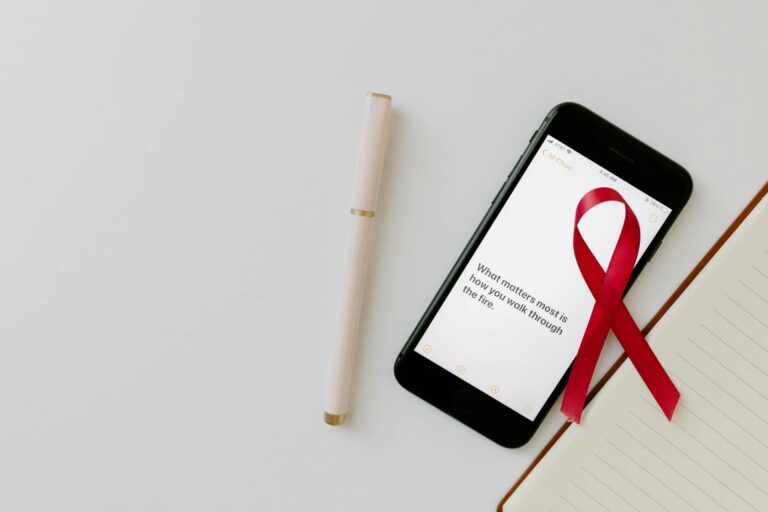 Image of a red awareness ribbon on a smartphone alongside a pen and notebook, symbolizing cancer awareness and advocacy.