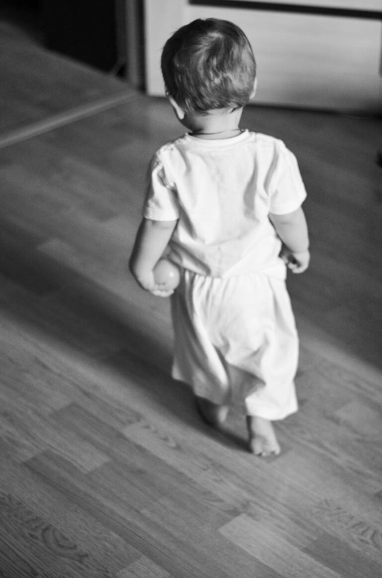 Black and white photo of a toddler walking indoors. Captures innocence.