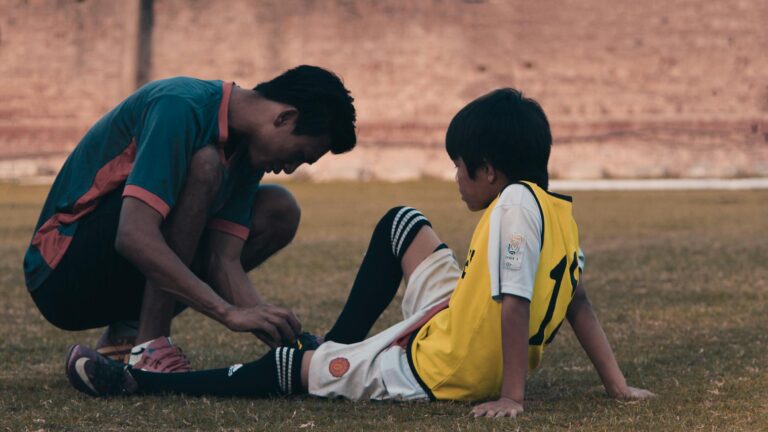 A young man helps a child with soccer gear during practice on a sunny day.