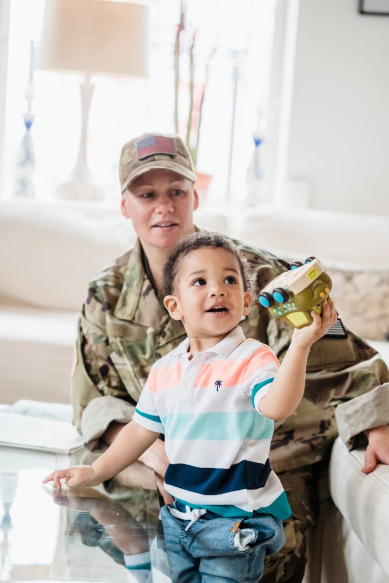 A young boy joyfully plays with a toy while his military parent watches in a cozy living room.