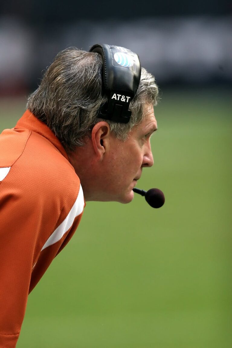 Side profile of a focused male football coach wearing a headset during a game.
