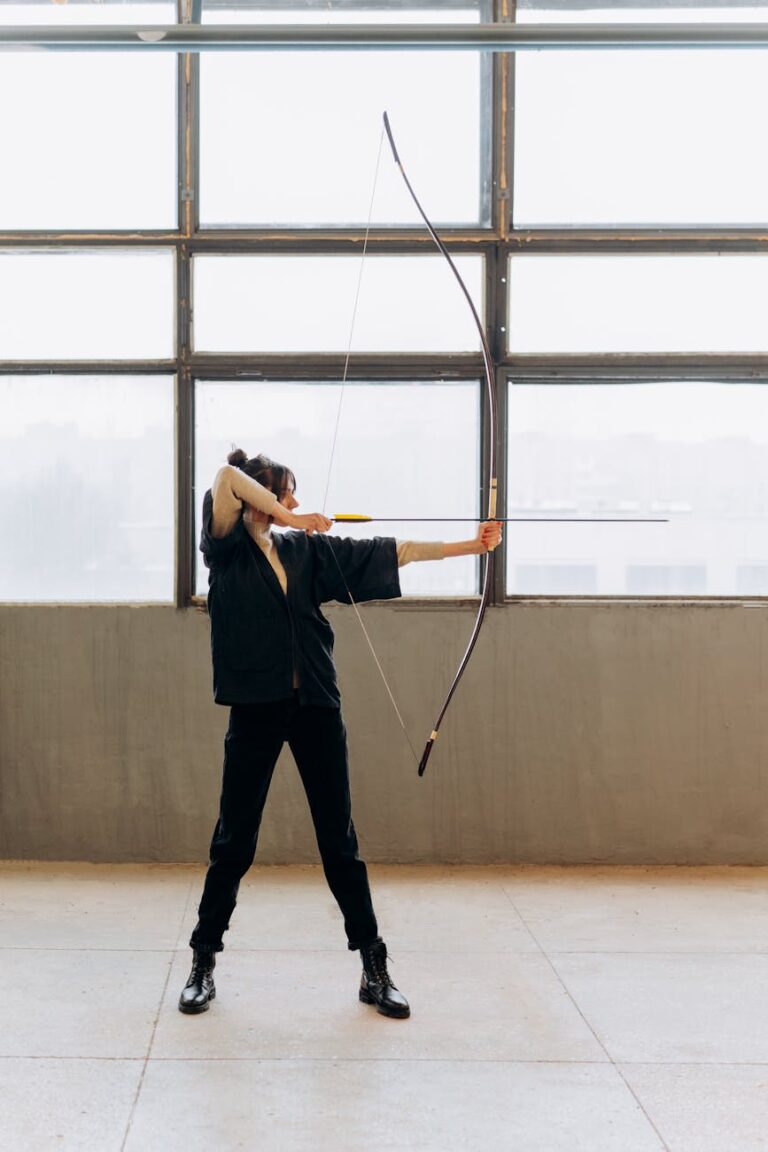 A determined young woman practicing archery indoors, showcasing focus and strength.