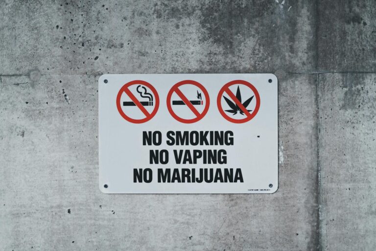 A clear warning sign prohibiting smoking, vaping, and marijuana on a concrete wall.