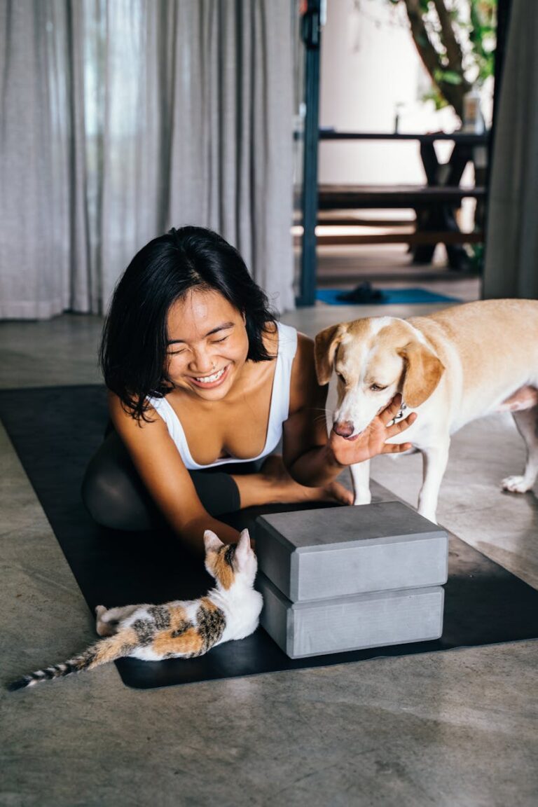 Smiling woman with dog and cat relaxing on a yoga mat indoors.