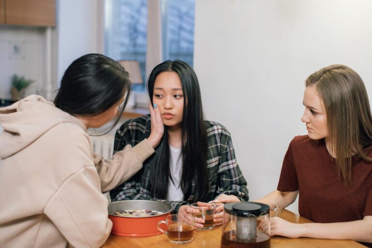Three women at a table offering emotional support and comfort to a friend, fostering compassion and empathy.