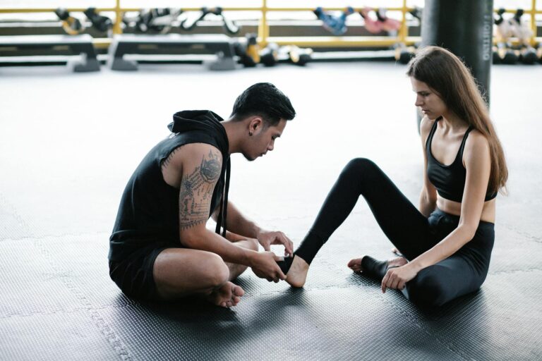A personal trainer helps a woman with an ankle bandage in a gym setting.