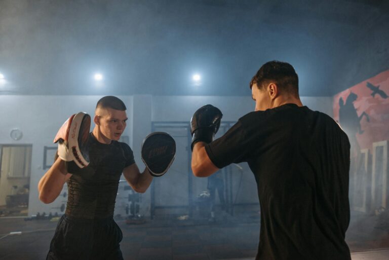 Two men engaged in boxing training indoors, showcasing focus and athleticism.