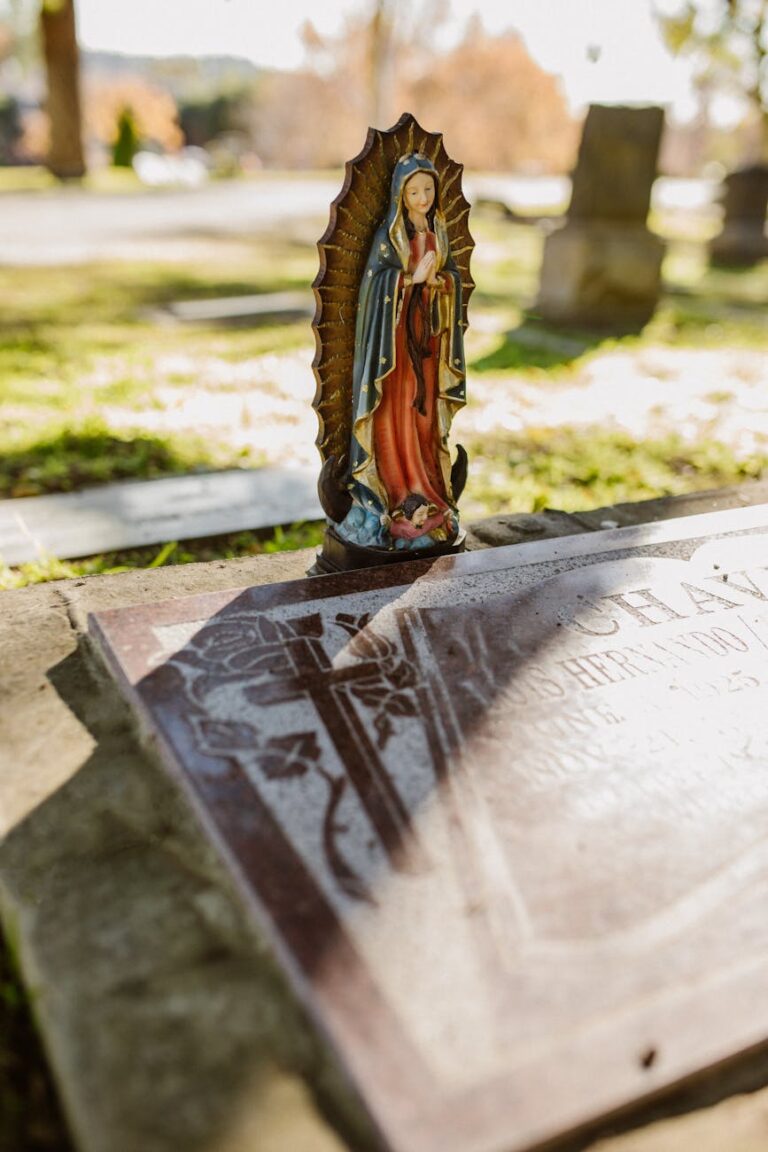 Statue of Virgin Mary on a gravestone in a sunlit cemetery, symbolizing spirituality and remembrance.