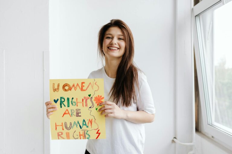 Smiling woman holding a colorful sign advocating for women's rights in a bright indoor setting.