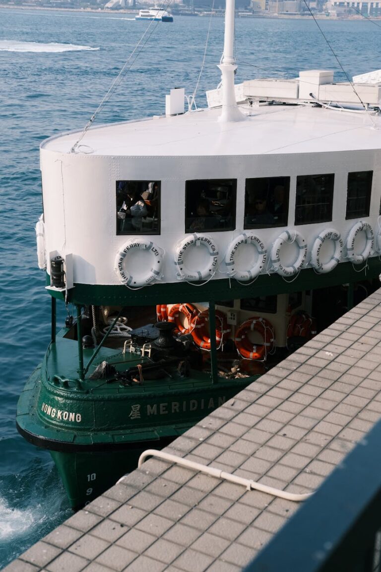A green passenger ferry navigating Victoria Harbour in Hong Kong with a distant cityscape view.